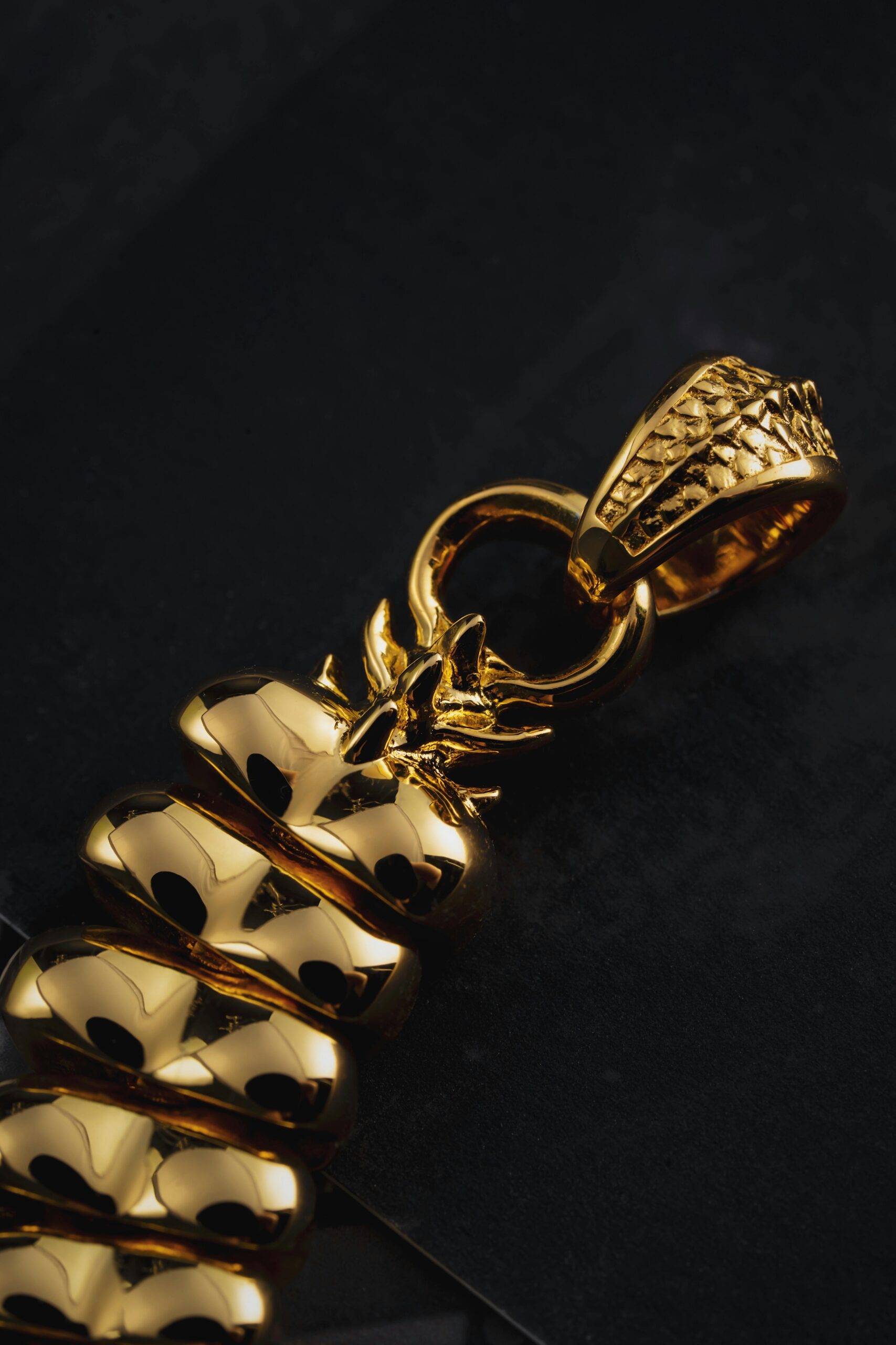 Close-up of a golden snake chain pendant against a black background.